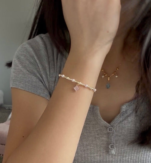Person wearing a pearl bracelet with small charms, gray shirt, and necklace.