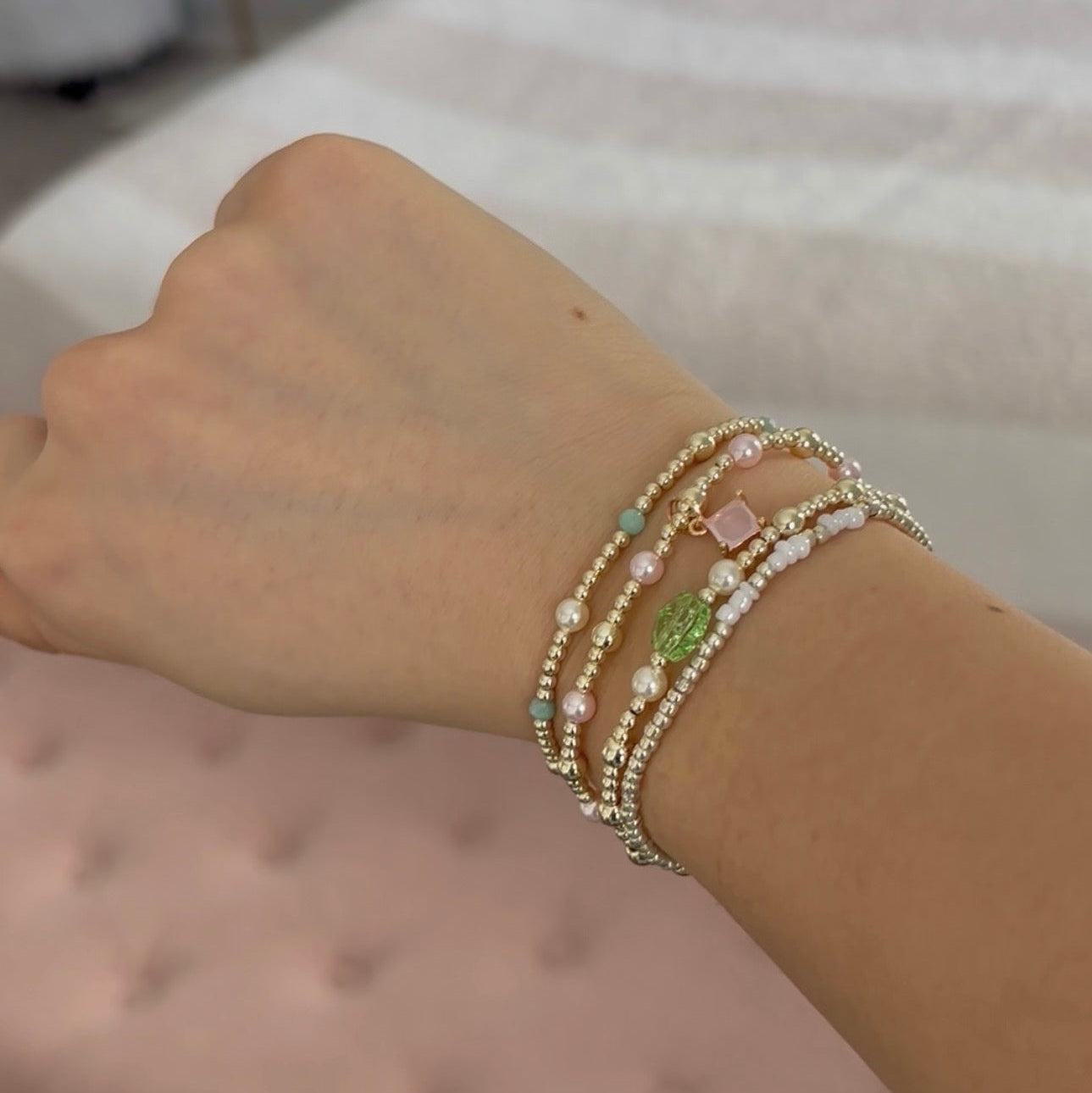 Wrist with multiple beaded bracelets on a neutral background