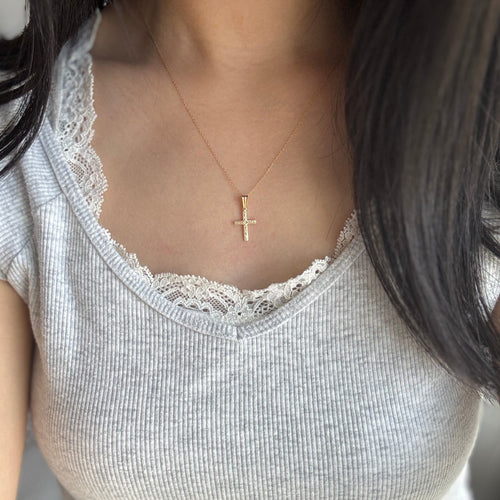 Person wearing a white lace-trimmed top with a gold necklace featuring a cross pendant.
