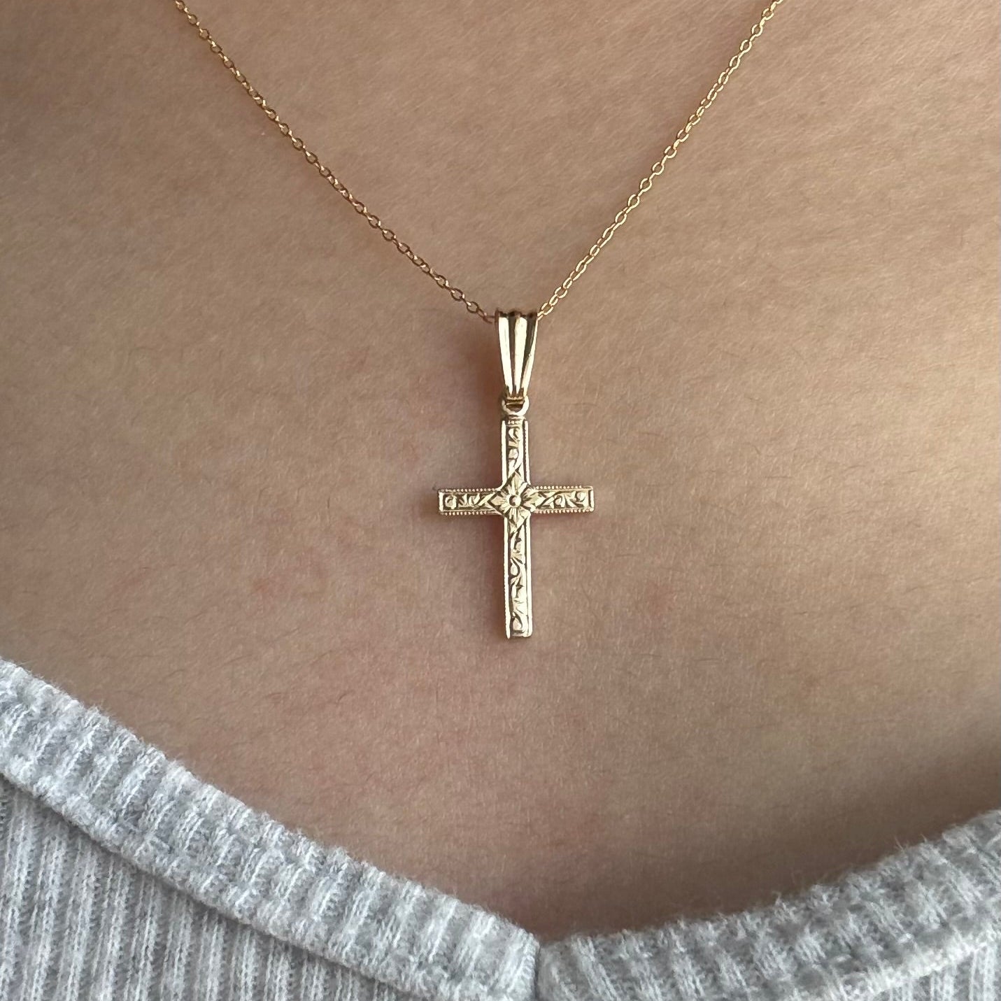Gold cross necklace on a person wearing a gray sweater.
