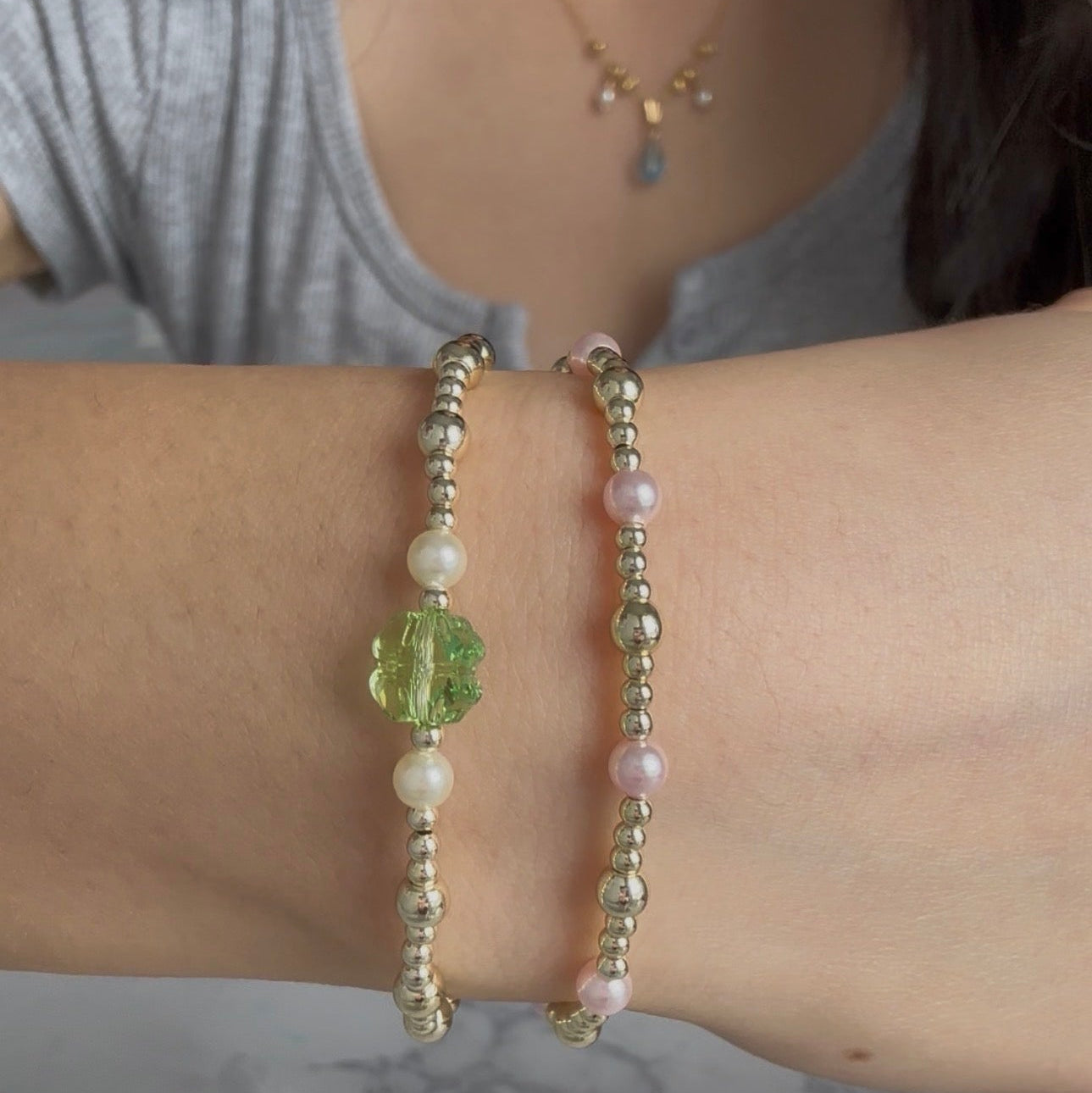 Close-up of a person's arm wearing two beaded bracelets with a gray shirt in the background.