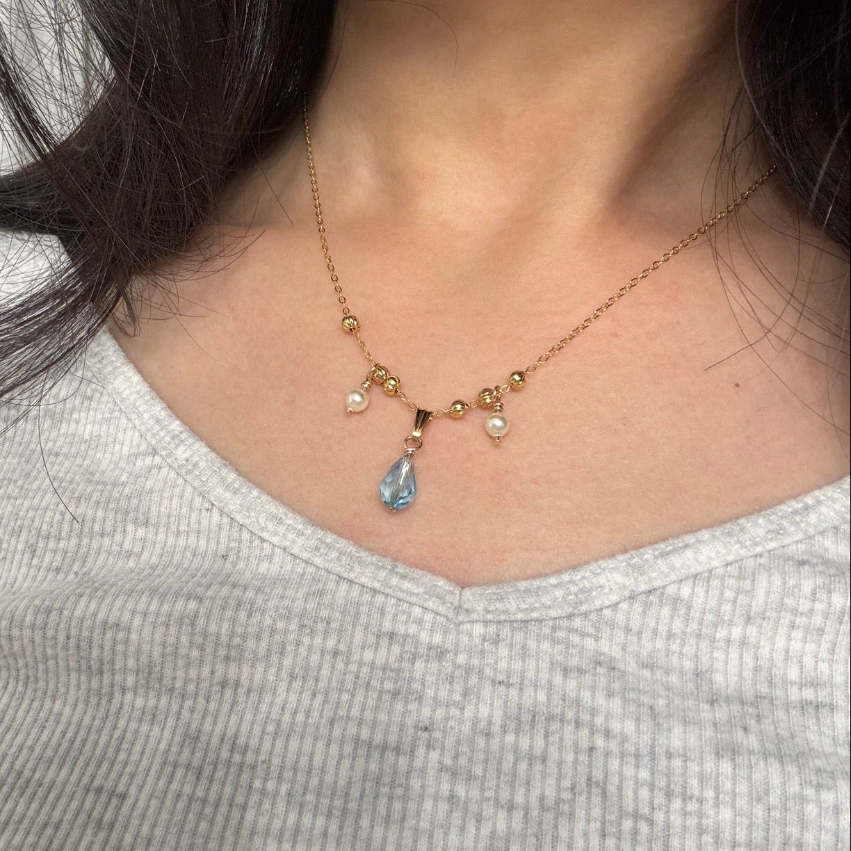 Necklace with a blue teardrop pendant and pearl drops worn by a person.