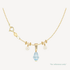Gold necklace with a blue teardrop pendant and pearl accents on a white background